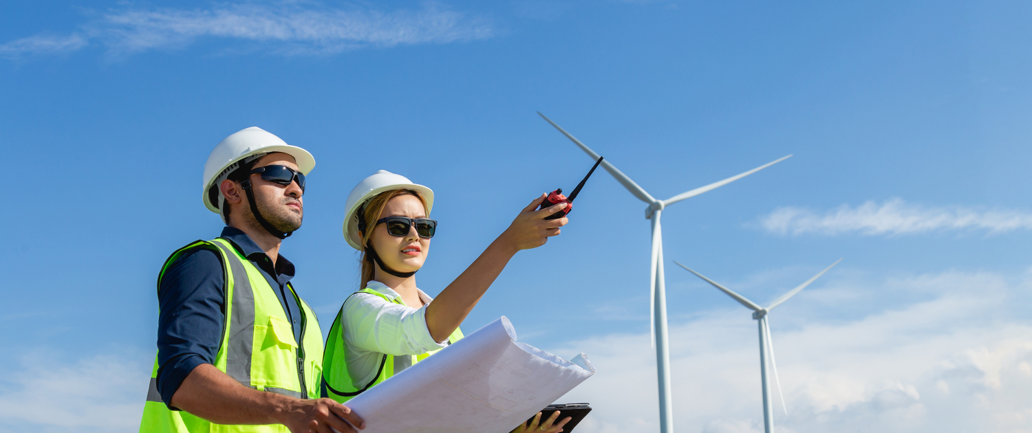Asian man and woman engineers working on site with copy space in wind turbine on the background. Young people engineers working at renewable energy farm